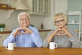 Smiling mature loving couple sitting and showing hearts with fingers