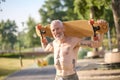 Smiling mature man holding longboard in a city park.