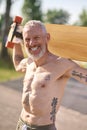 Smiling mature man holding longboard in a city park.