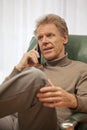 Smiling mature man talking on smartphone in a chair in a living room