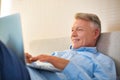 Smiling mature man using laptop while lying on bed at home Royalty Free Stock Photo