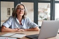 Smiling mature middle aged woman sitting at workplace with laptop, portrait. Royalty Free Stock Photo