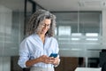 Smiling mature professional business woman entrepreneur using phone in office. Royalty Free Stock Photo