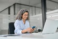 Smiling mature business woman holding phone using cellphone in office. Royalty Free Stock Photo