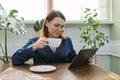 Smiling mature woman having breakfast at home reading digital tablet Royalty Free Stock Photo