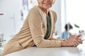 Smiling mature woman leans onto cutting table in spacious sewing workshop, closeup