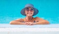 Smiling mature woman in outdoor swimming pool standing near the edge with sunglasses and straw hat. summer and vacation concept Royalty Free Stock Photo