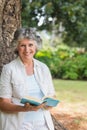 Smiling mature woman reading book leaning on tree trunk Royalty Free Stock Photo