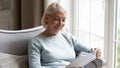 Happy elderly woman reading book relaxing at home