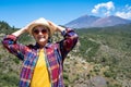 Smiling mature woman with straw hat standing outdoors enjoying hike. Mountains with the Teide volcano in the background Royalty Free Stock Photo