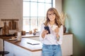 Smiling mature woman text messaging and drinking coffee while standing at her kitchen in the morning Royalty Free Stock Photo