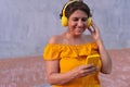 Smiling mature woman using cell phone while listening to music with headphones against wall Royalty Free Stock Photo