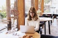 Smiling mature woman using laptop and working while sitting at the cafe