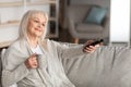 Smiling mature woman watching tv holding remote control and cup Royalty Free Stock Photo