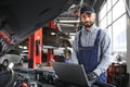 Smiling mechanic using a laptop pc at the repair garage. Royalty Free Stock Photo