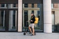 Smiling messneger man standing outdoors with electric push scooter. Delivery man with termal backpack in the city