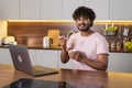 A smiling mestizo young man in the kitchen in subdued lighting, holds a bowl of pasta in hands, wraps them in a fork. An