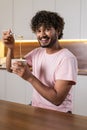 A smiling mestizo young man in the kitchen in subdued lighting, holds a bowl of pasta in hands, wraps them in a fork. An