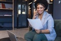 Smiling mid adult biracial businesswoman talking on smart phone while reading document in office Royalty Free Stock Photo