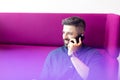 Smiling mid adult businessman talking on mobile phone while sitting on purple couch at office Royalty Free Stock Photo