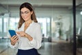 Smiling mid aged business woman holding cell phone standing in office. Royalty Free Stock Photo