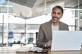 Smiling middle aged business man sitting at desk using laptop looking away. Royalty Free Stock Photo