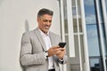 Smiling middle aged business man standing outdoors using mobile phone. Royalty Free Stock Photo