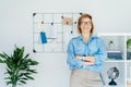 Smiling middle aged businesswoman near grid mood board with pinned work-life balance wheel diagram in her work space