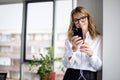Close-up of middle aged smiling business woman using smartphone and earphone in a modern office Royalty Free Stock Photo