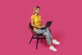 Smiling middle aged caucasian woman blonde in casual sits on chair, typing on laptop Royalty Free Stock Photo