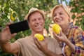 Smiling middle-aged couple holding lemons, making selfie