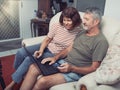 Smiling middle aged couple sitting on their couch using the laptop to buy online at home Royalty Free Stock Photo