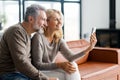 Smiling middle-aged couple using smartphone sitting on the comfortable sofa Royalty Free Stock Photo