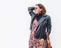 Smiling middle-aged female dressed boho fashion style colorful long dress with black leather biker jacket with brown leather flap