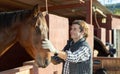 Smiling adult man stroking horse on animal ranch on autumn sunny day Royalty Free Stock Photo