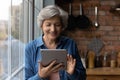 Smiling middle aged latin female use tablet computer at kitchen