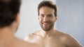 Smiling middle-aged man admiringly looking at his reflection in mirror