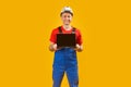 Smiling middle aged man architect engineer in safety helmet holding laptop with empty screen. Yellow studio background. Copy space Royalty Free Stock Photo