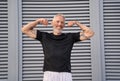 Smiling middle aged man raised his arms and shows his biceps while posing outdoors over gray background Royalty Free Stock Photo