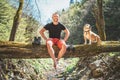 Smiling middle-aged man sitting on the fallen tree log over the mountain forest stream with his beagle dog while he waiting for Royalty Free Stock Photo