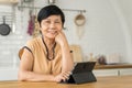 Smiling middle aged mature Asian woman looking at camera while using digital tablet. Portrait of beautiful senior female at home Royalty Free Stock Photo