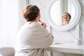 Smiling middle aged plus size woman doing makeup near mirror at home Royalty Free Stock Photo