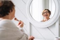 Smiling middle aged plus size woman doing makeup near mirror at home Royalty Free Stock Photo
