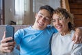 Smiling middle-aged 40s mother rest with grown-up son using smartphone together, happy young man enjoy family weekend with mom Royalty Free Stock Photo
