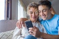 Smiling middle-aged 40s mother rest with grown-up son using smartphone together, happy young man enjoy family weekend with mom Royalty Free Stock Photo