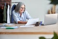 Middle aged stylish woman fashion designer holding sketches in studio office. Royalty Free Stock Photo