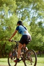 Smiling middle aged woman in cap with glasses cycling in summer park, rear view, cycling cardio training, walking in the Royalty Free Stock Photo