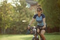 Smiling middle aged woman in cap with glasses cycling in summer park, cycling cardio training, city walks with bike Royalty Free Stock Photo