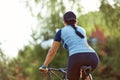 Smiling middle aged woman in cap with glasses cycling in summer park, rear view, cycling cardio training, walking in the Royalty Free Stock Photo
