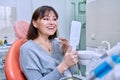 Smiling middle aged woman in dental chair with mirror looking at her teeth Royalty Free Stock Photo